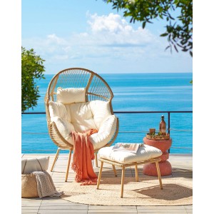 Beiger Rattansessel mit Fußhocker und weißen Kissen vor blauem Meer. Gartenstuhl für entspannte Stunden.