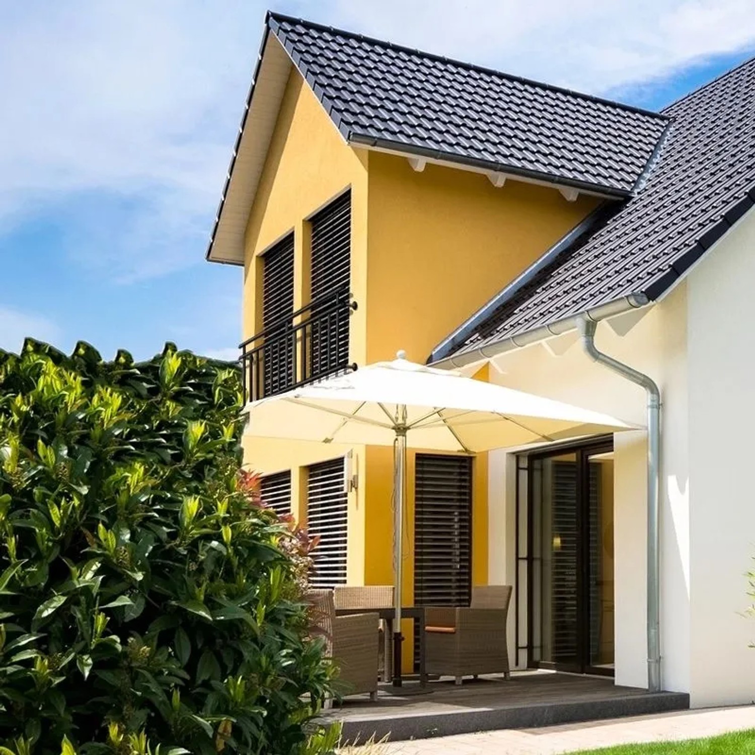 Schwarzer französischer Balkon aus Stahl mit 16 Füllstäben an gelbem Haus. Robuste Fenstersicherung.