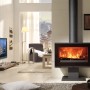 Panadero Maja-S Kaminofen, Stahl schwarz metallic, 7 kW, im Wohnraum mit brennendem Feuer.