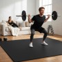 Schwarze Bodenschutzmatte im Home Gym. Mann trainiert mit Langhantel, Frau entspannt. Robuste Fitnessmatte für Sportgeräte.