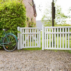 Weißer Vorgartenzaun Country aus Nadelholz, 150x96 cm, mit geöffnetem Gartentor und Fahrrad im Garten.