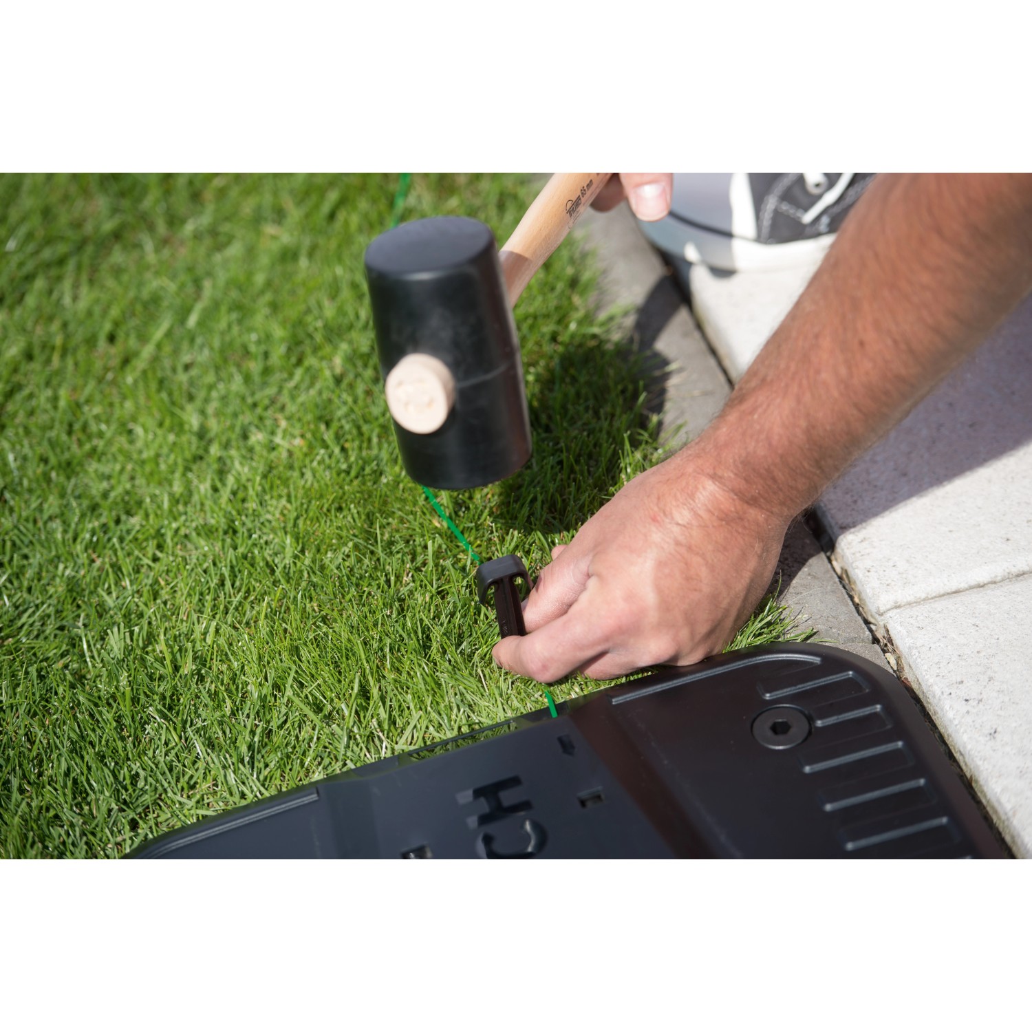 Bosch Fixierstifte für Indego Begrenzungsdraht werden mit Hammer in den Rasen geschlagen.