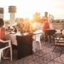 Rechteckiger schwarzer Klapp-Gartentisch aus Kunststoff auf Terrasse, Freunde grillen und essen bei Sonnenuntergang.
