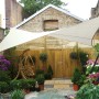 Cremefarbenes Perel Viereck-Sonnensegel 500x500 cm spendet Schatten im Garten.