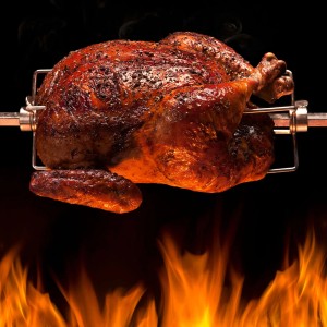 Knuspriges Grillhähnchen am Taino Drehspieß für Gasgrill, mit Flammen im Vordergrund.