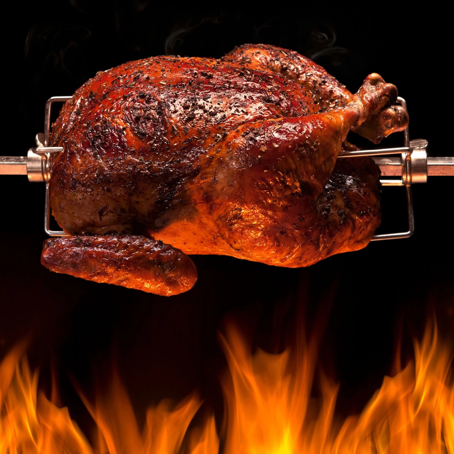 Knuspriges Grillhähnchen am Taino Drehspieß für Gasgrill, mit Flammen im Vordergrund.