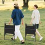 Zwei Personen tragen zusammengeklappte, schwarze Costway Gartenstühle mit Armlehnen.