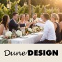 Feiernde Gruppe stößt an festlich gedecktem Tisch im Freien an, mit DuneDESIGN Logo.