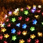 Bunte LED Solar-Lichterkette mit Kirschblüten auf einem dunklen Busch, ideal für Weihnachtsbeleuchtung im Garten.