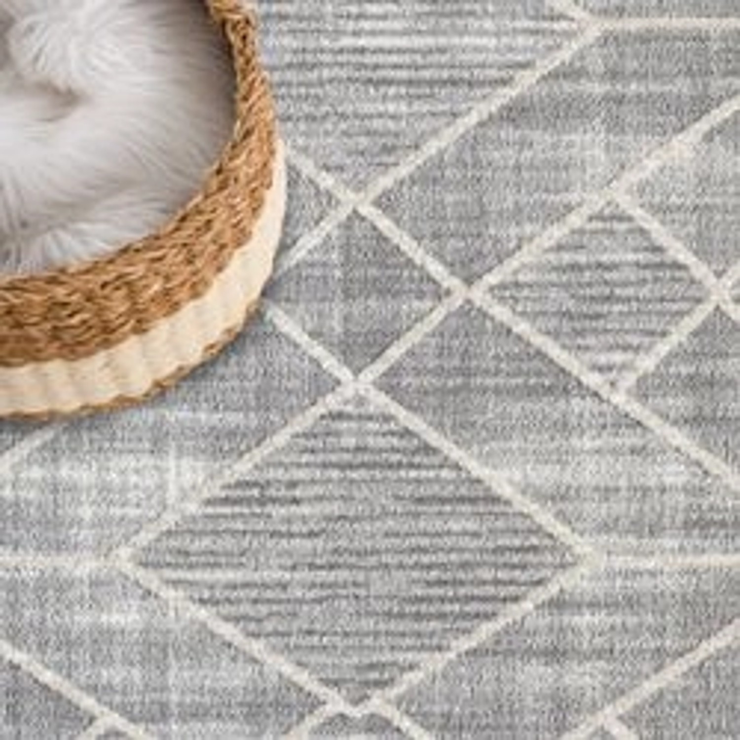 Grauer Hochflor Teppich Esso (200x290 cm) mit Rautenmuster und Korb im Hintergrund.