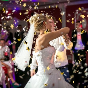 Goldener Sternenregen Konfetti fällt über tanzendes Brautpaar. Partypopper für Hochzeit, Geburtstag, Feier.