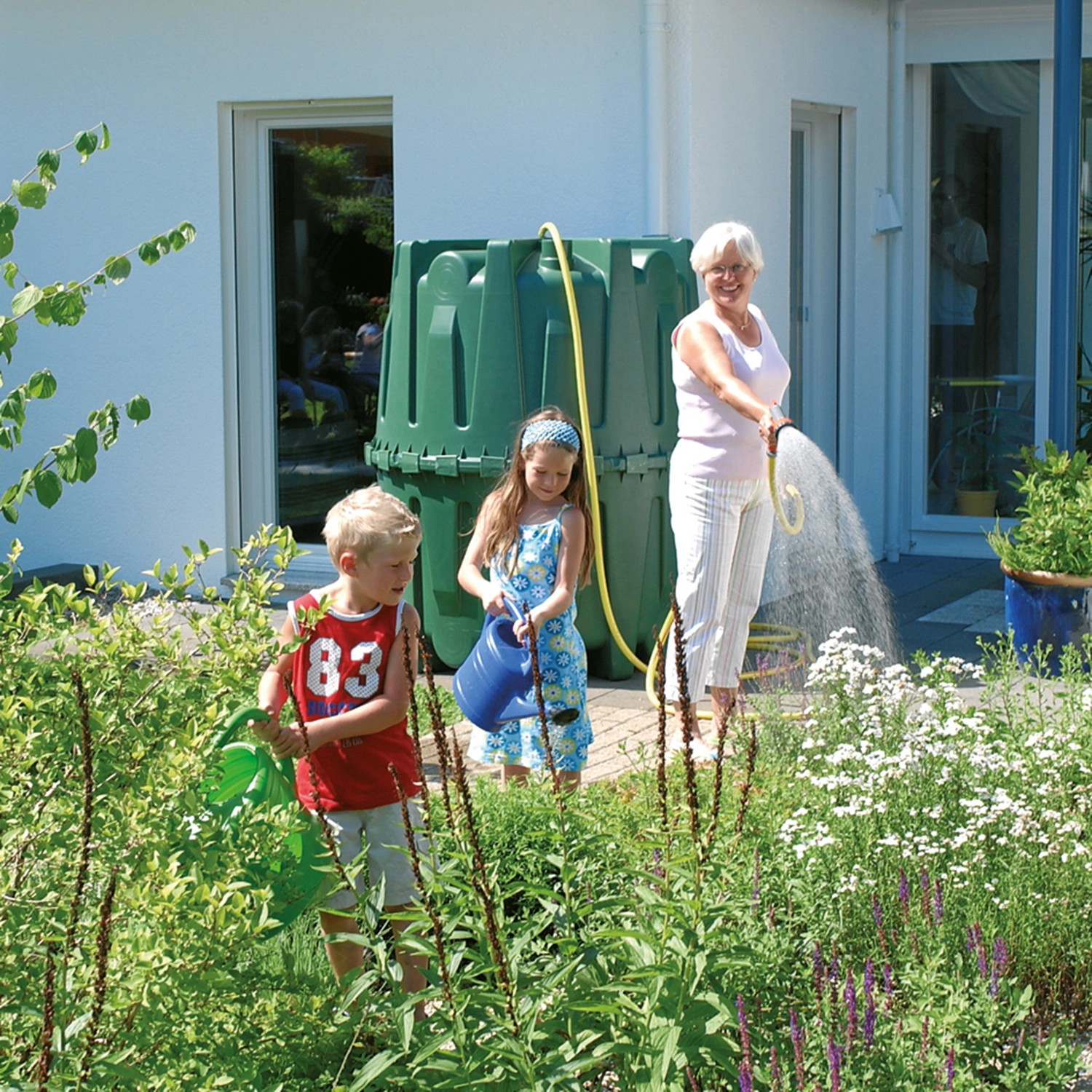 Garantia Zisterne Herkules 1600 l im Garten mit spielenden Kindern und Frau beim Gießen.