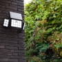 Schwarze Lutec LED-Solarleuchte Tuda mit 3 Leuchten an einer Backsteinwand.