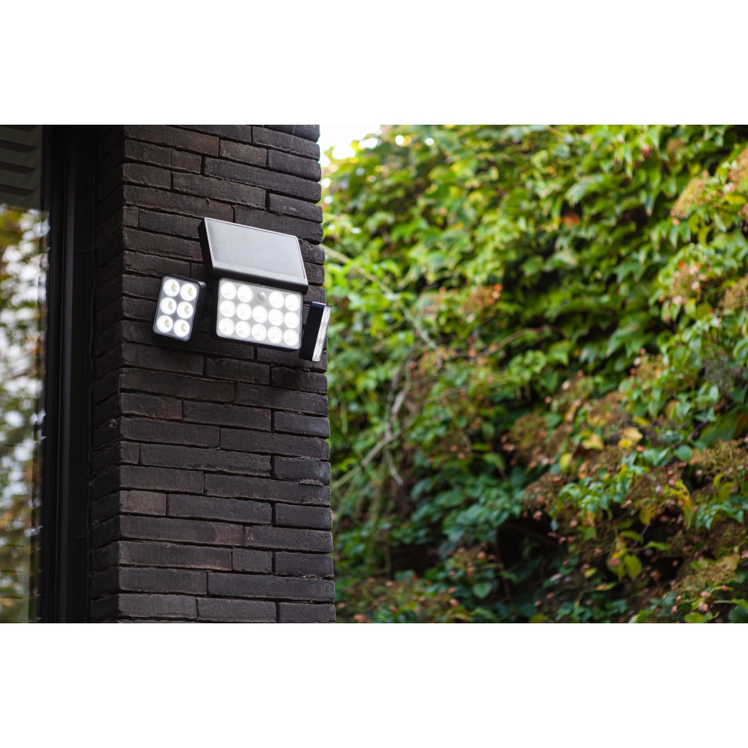 Schwarze Lutec LED-Solarleuchte Tuda mit 3 Leuchten an einer Backsteinwand.