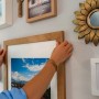 Frau befestigt Bilderrahmen mit Tesa Powerstrips Click an Wand. Klebenägel für sicheren Halt.