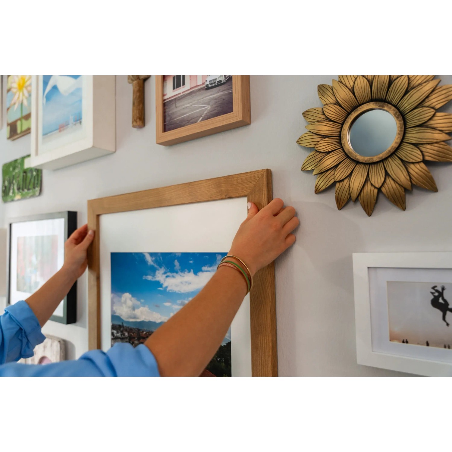 Frau befestigt Bilderrahmen mit Tesa Powerstrips Click an Wand. Klebenägel für sicheren Halt.