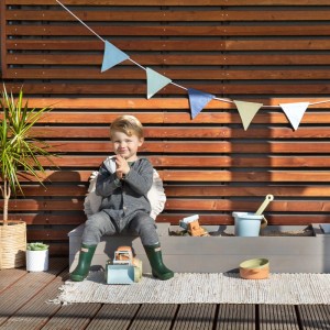 Kind sitzt am MUDDY BUDDY Sandkasten Space Saver in Warmgrau mit Spielzeug.