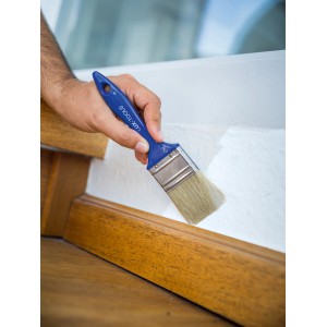 Hand streicht mit LUX Flachpinsel (30mm) weiße Wand. Pinsel mit blauem Griff.