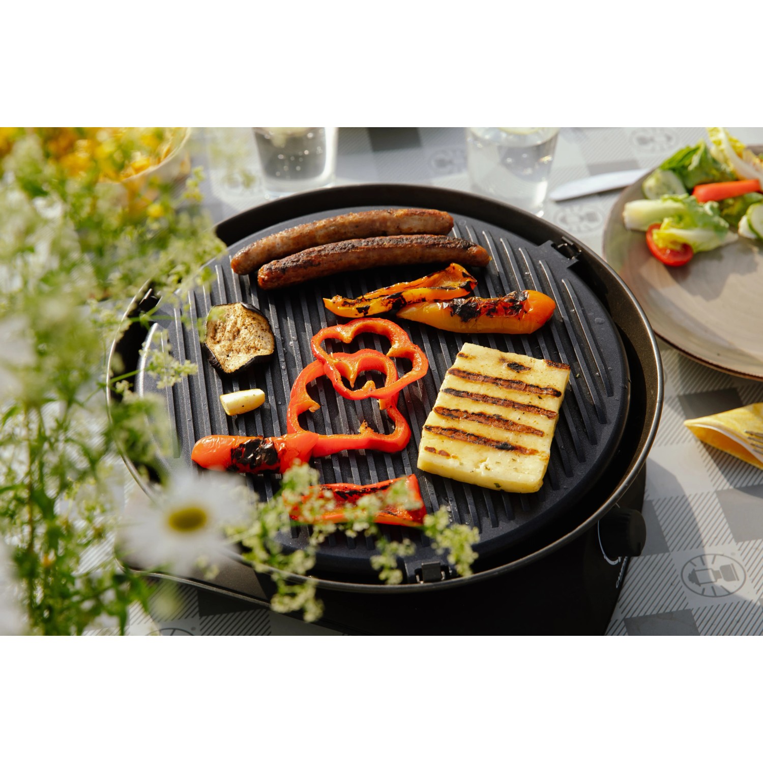 Campingaz 360° Tischgrill Anthrazit mit Grillgut wie Würstchen, Gemüse und Halloumi.