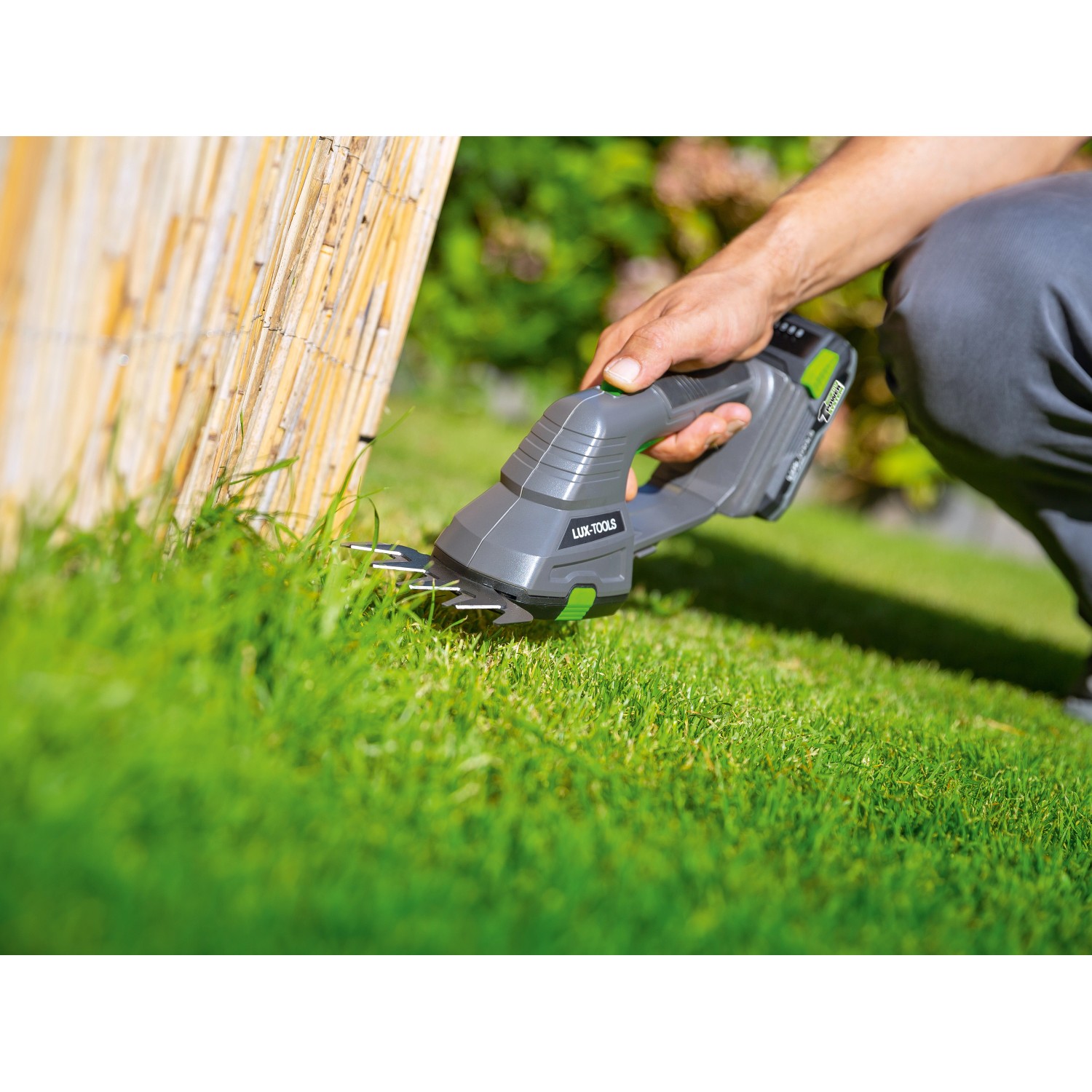 LUX Akku-Grasschere im Einsatz zum Kantenschneiden, graues Gehäuse, grüne Akzente.