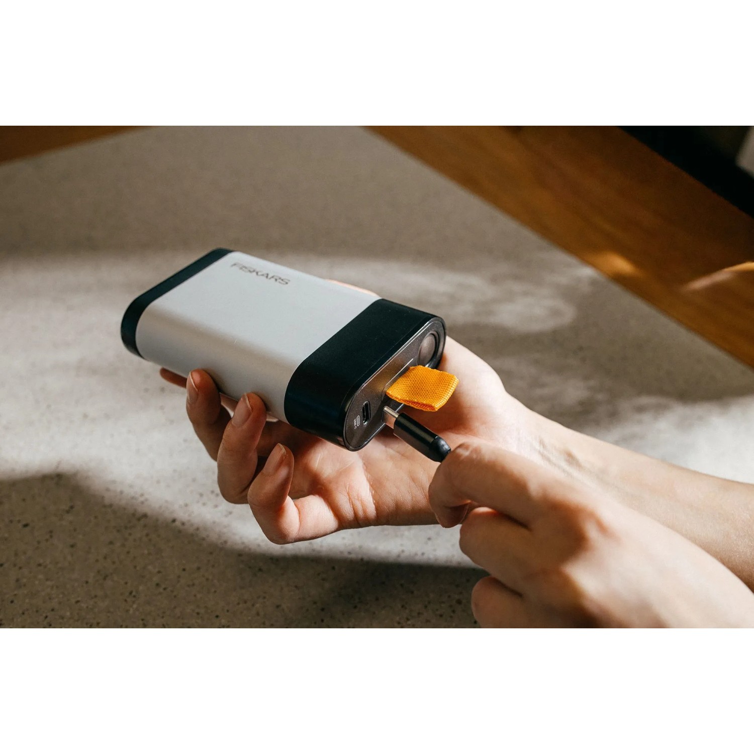 Hand lädt Fiskars 12V 4Ah Akku mit USB-C Kabel. Kompakte, weiß-schwarze Powerbank für Gartengeräte.