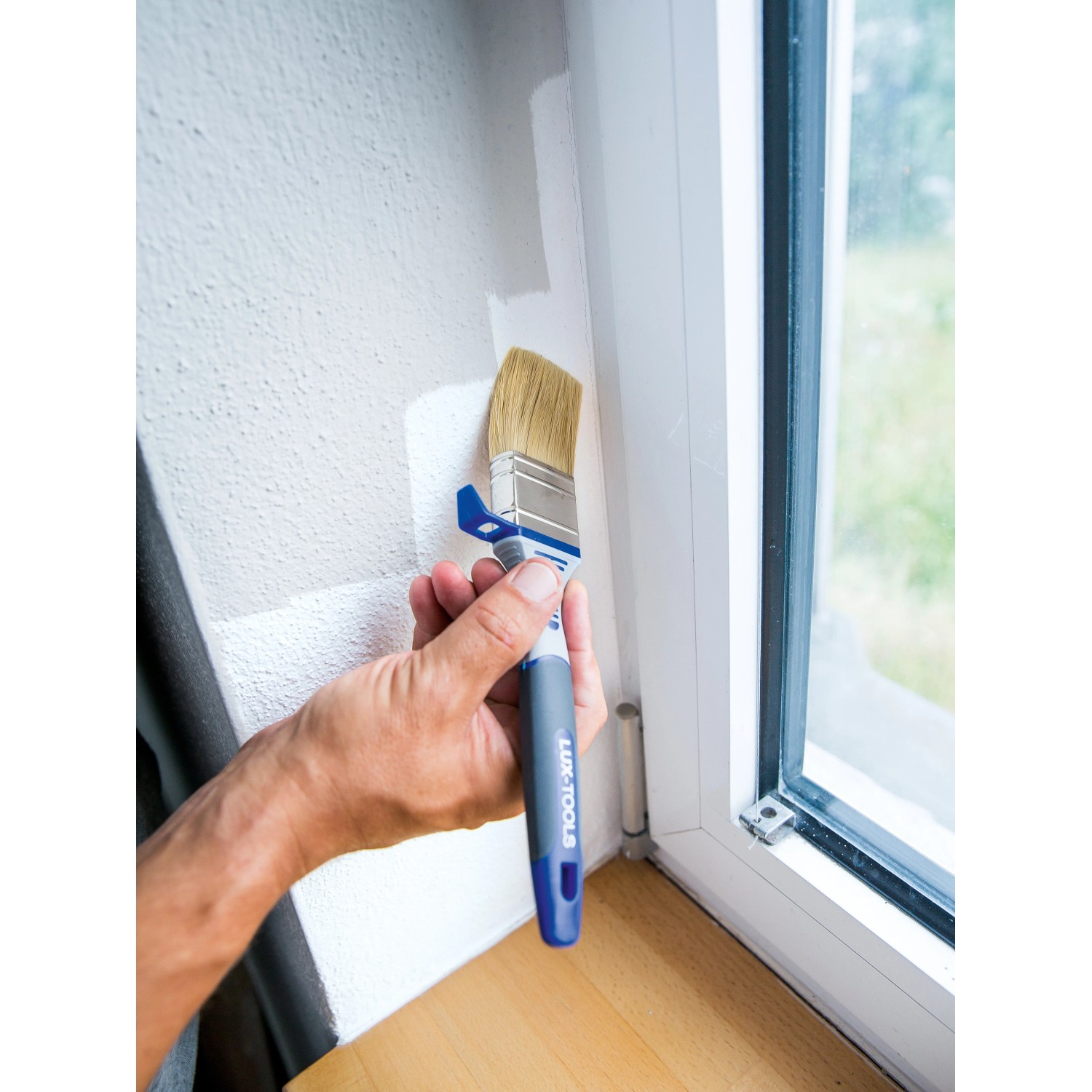 LUX Flachpinsel 40mm beim Streichen einer Wand, Detailaufnahme des Pinsels mit Eimerhaken.