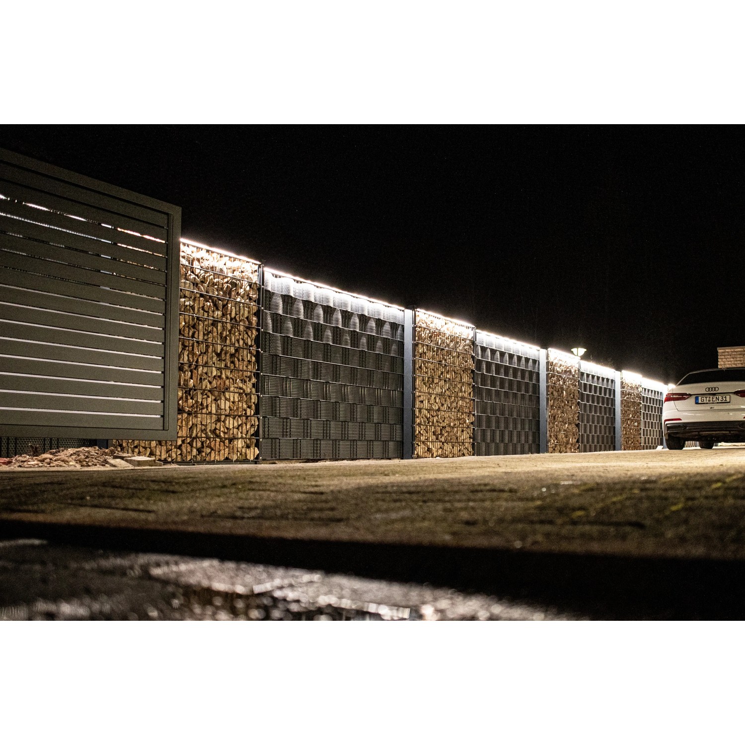 LyghtUp LED-Zaunbeleuchtung Set in Silber an einem Zaun mit Gabionen und einem Tor.