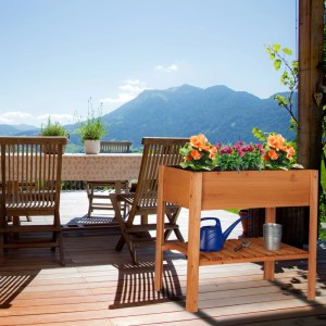 Rotbraunes Tannenholz Hochbeet mit bunten Blumen und Ablagefach, auf einer sonnigen Terrasse mit Bergblick.