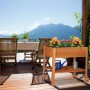 Rotbraunes Tannenholz Hochbeet mit bunten Blumen und Ablagefach, auf einer sonnigen Terrasse mit Bergblick.