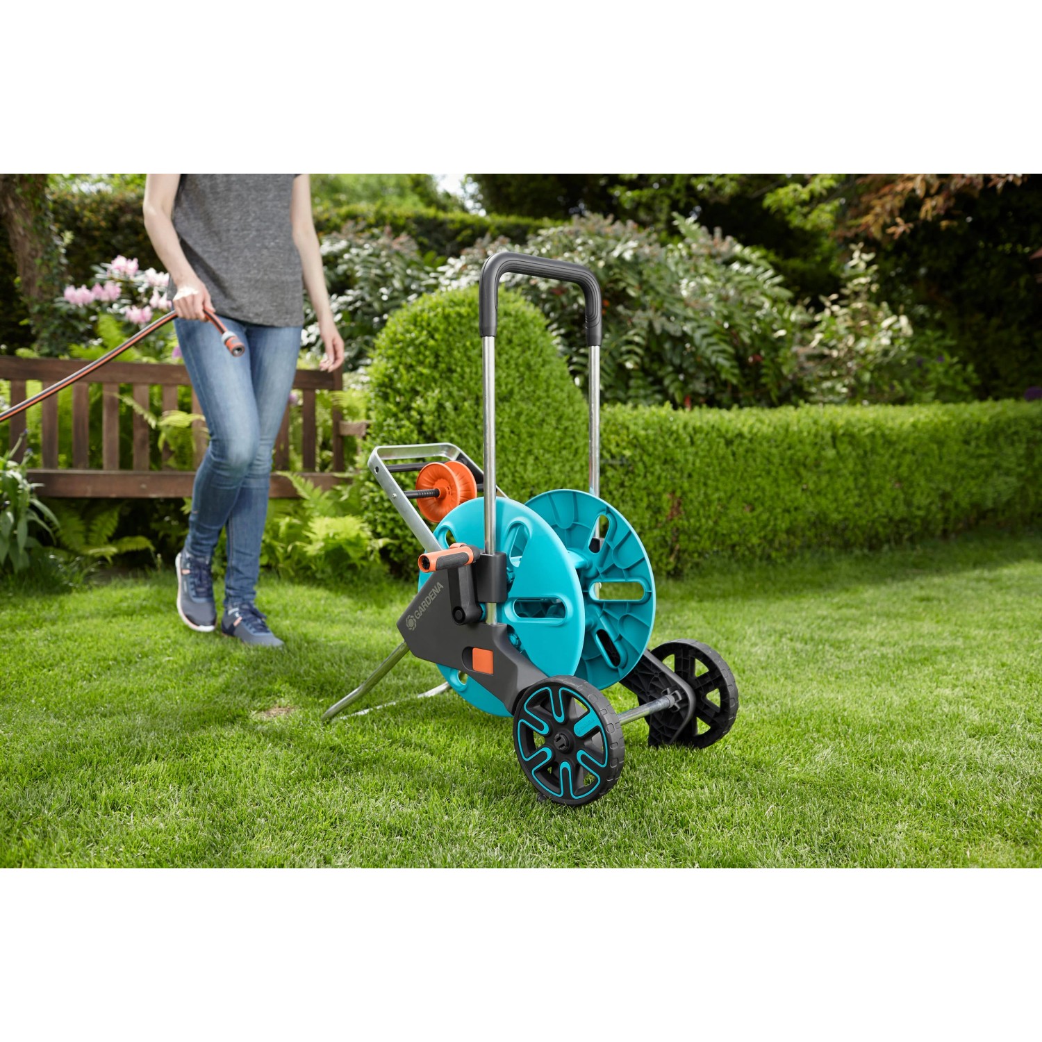 Gardena CleverRoll M Easy Schlauchwagen mit Frau im Garten. Schlauchwagen ist blau/grau und hat Räder.