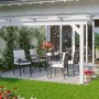 Weiße Skan Holz Terrassenüberdachung Ancona mit Sitzgruppe und Tisch im Garten.