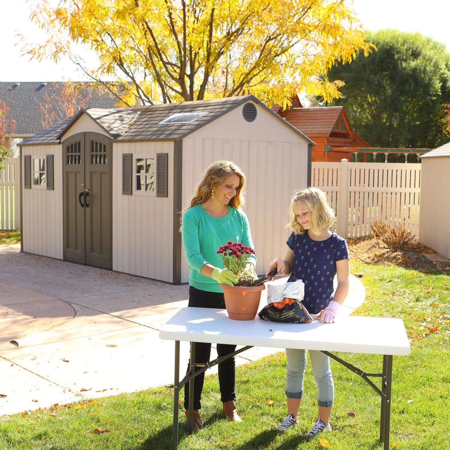 Lifetime Gerätehaus Castle 11,15 m² im Garten mit Mutter und Tochter beim Pflanzen.