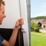 Mann bedient weißes Abus Fenstergriff-Schloss mit Alarm zur Fenstersicherung.