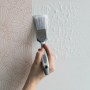 Hand streicht Tapetenkleister mit Pinsel auf Wand. Wallpro Werkzeug-Set für Vliestapeten.