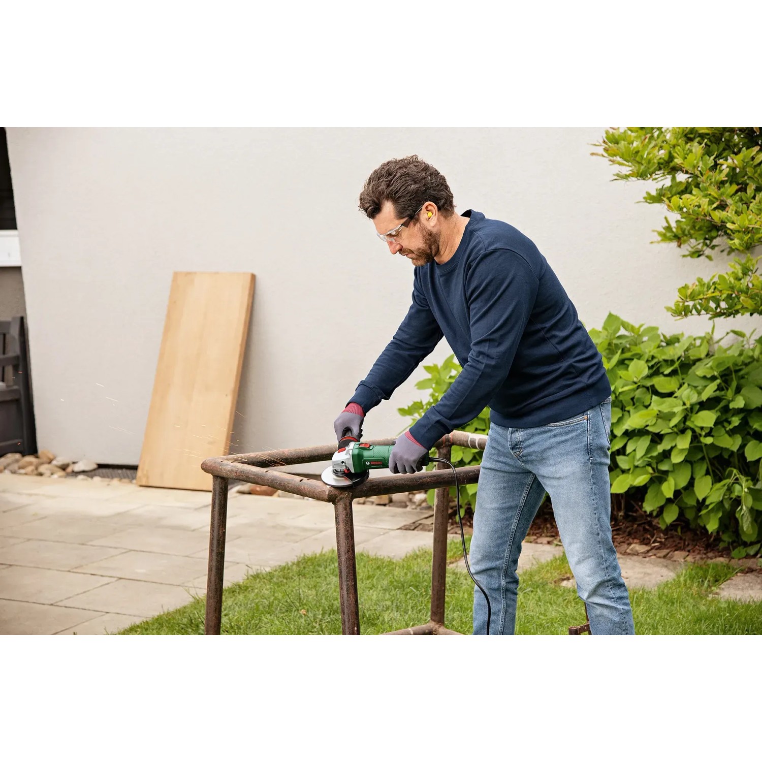 Mann schleift Metall mit Bosch UniversalGrind 850-125 Winkelschleifer im Garten.