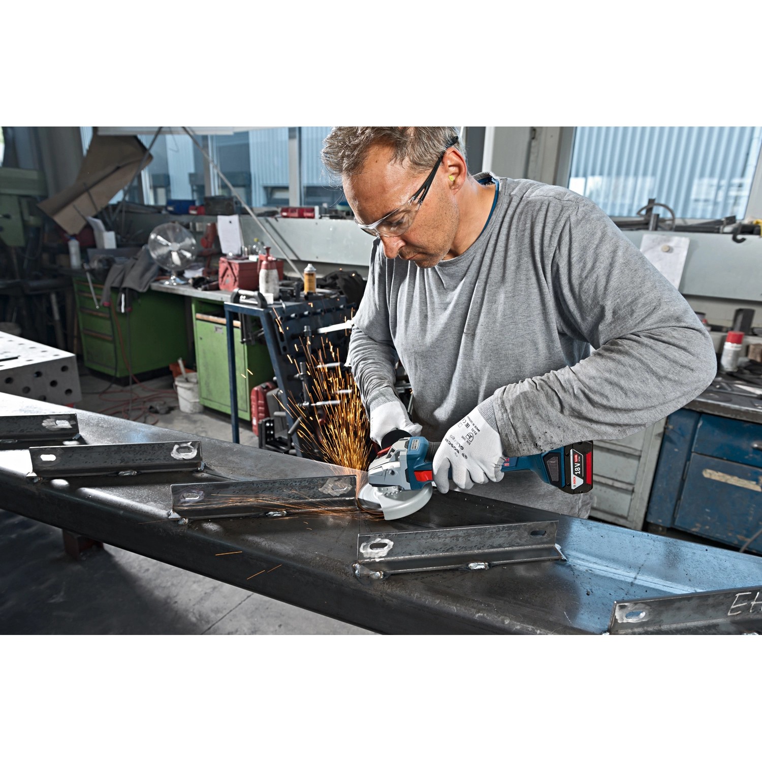 Mann schleift Metall mit Bosch Akku-Winkelschleifer aus dem Professional Combi-Kit. Funken fliegen.