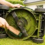 Mann reinigt grünen Rasenmäher mit Rasenmäher-Bürste und Schaber. Entfernt Grasreste vom Mähwerk.