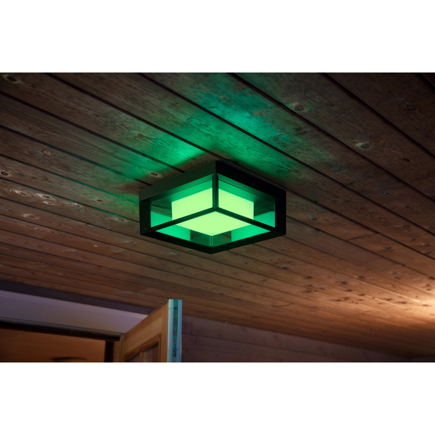 Quadratische Philips Hue Econic LED-Wandleuchte mit grüner Beleuchtung an einer Holzdecke.
