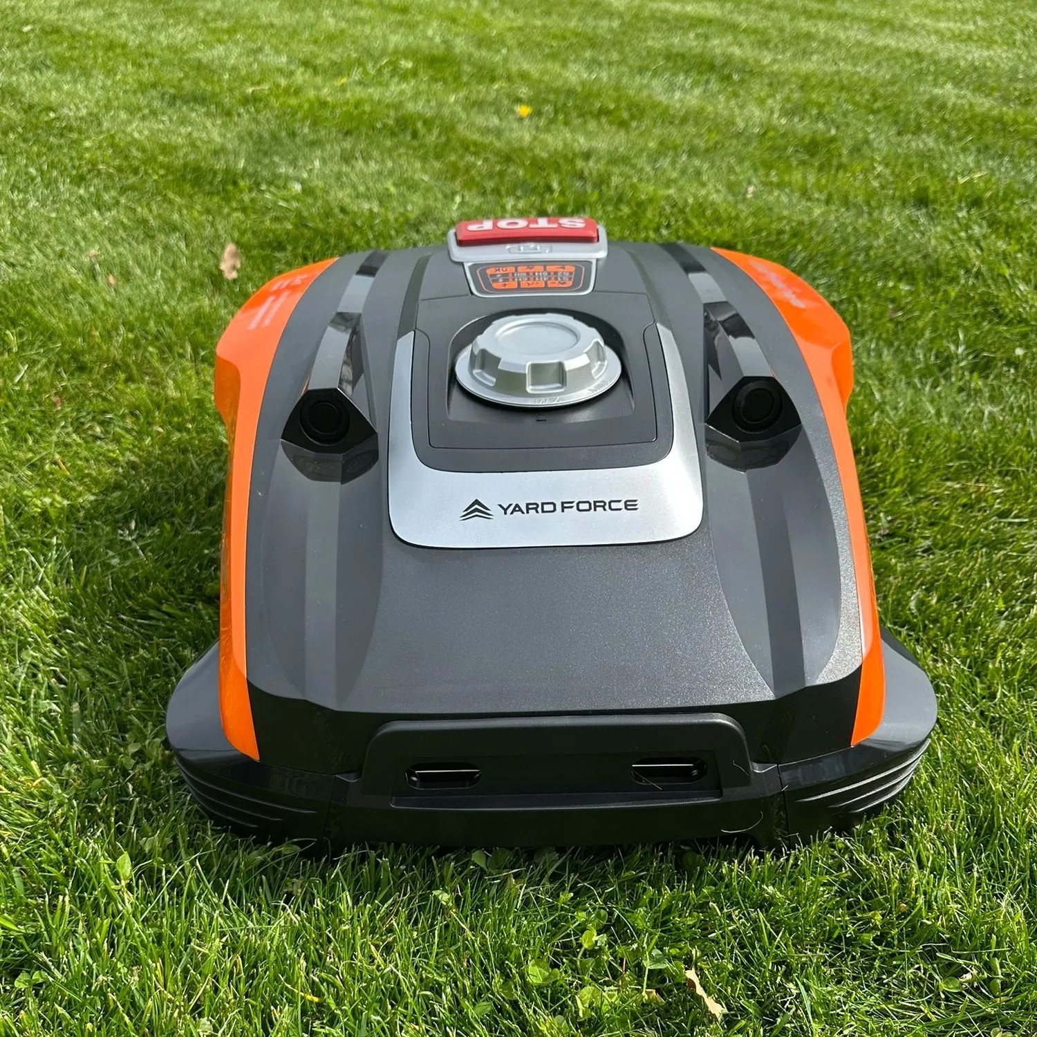 YARD FORCE Mähroboter Compact 300RBS in Orange-Grau auf Rasen. Mit STOP-Taste und Bedienfeld.