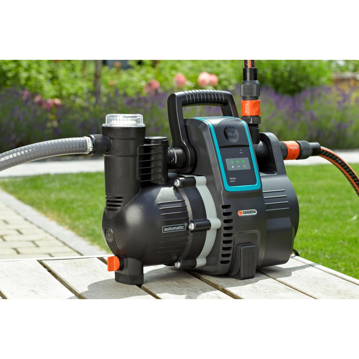 Gardena smart Haus- und Gartenautomat 5000/5 Set: Schwarze Gartenpumpe mit grauem Schlauch auf Holztisch.