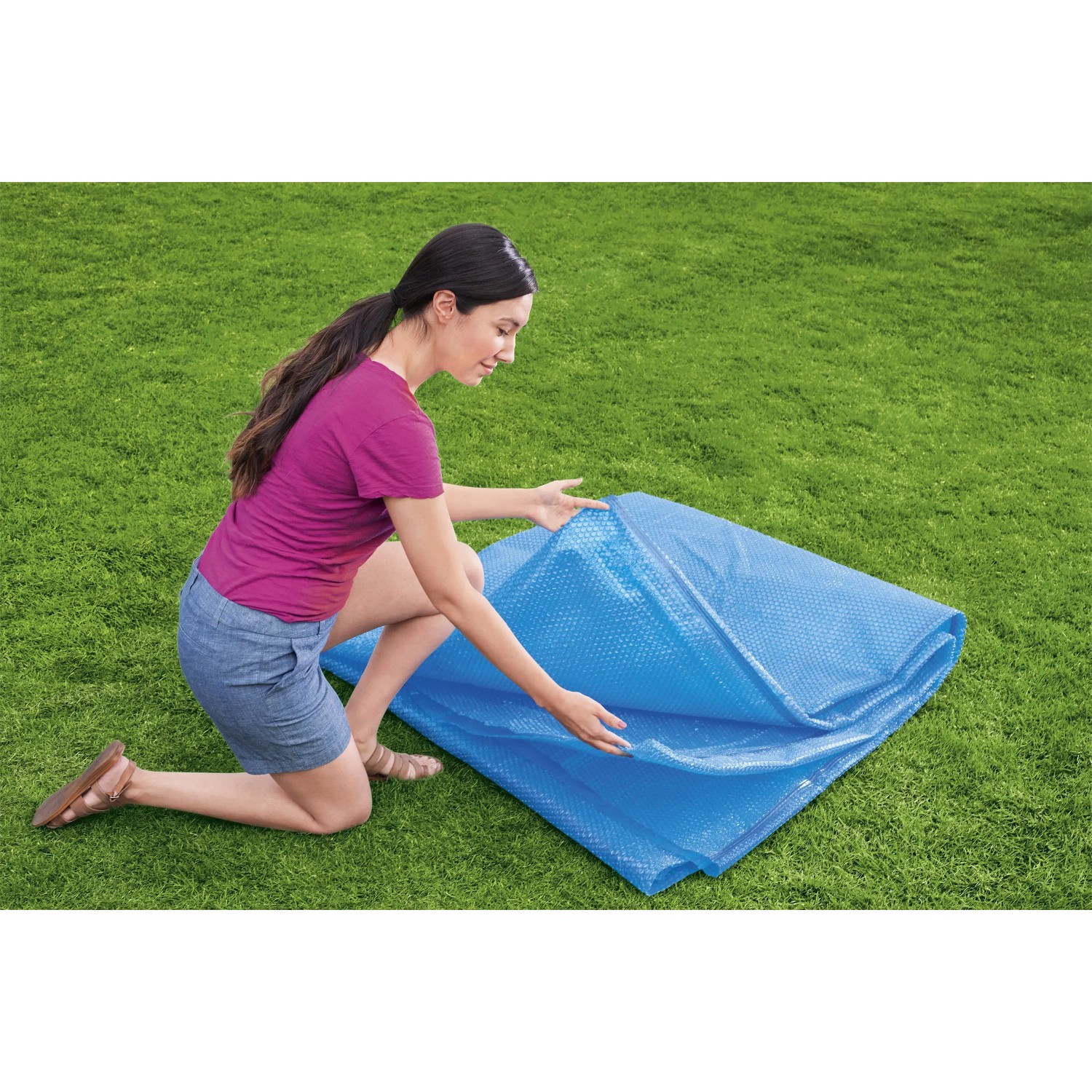 Bestway PE Solar Cover, blau, rechteckig, 703x336 cm. Frau legt Pool Abdeckplane auf Rasen.
