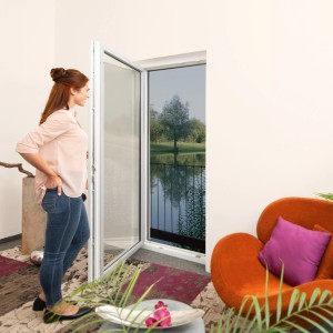 Frau betrachtet Windhager Insektenschutzgitter in Anthrazit am Fenster mit Blick ins Grüne.