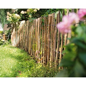 Natürlicher Staketenrollzaun aus unbehandelter Haselnuss im Garten.