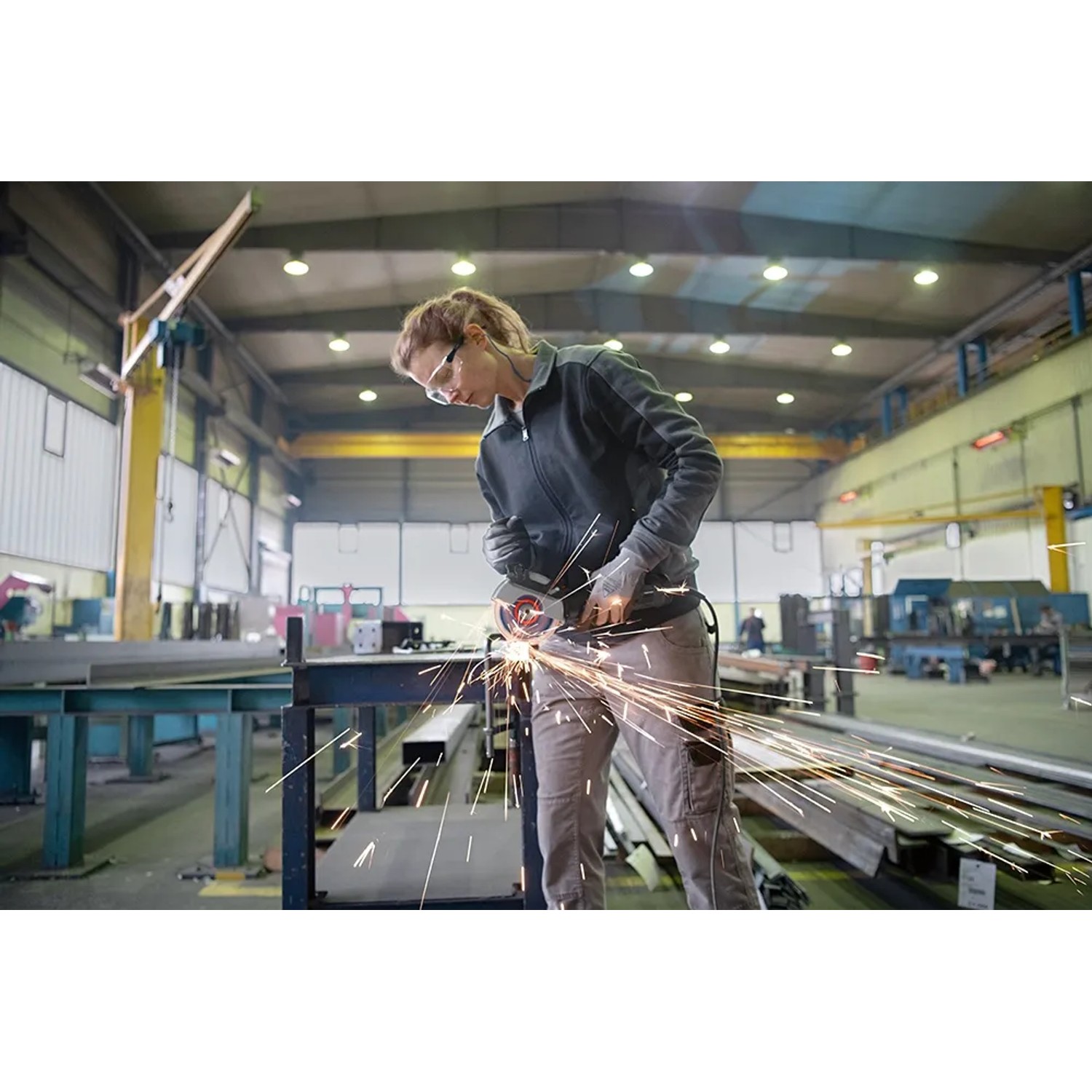 Frau schleift Metall mit dem Bosch Professional Winkelschleifer GWS 17-125 in einer Werkstatt.