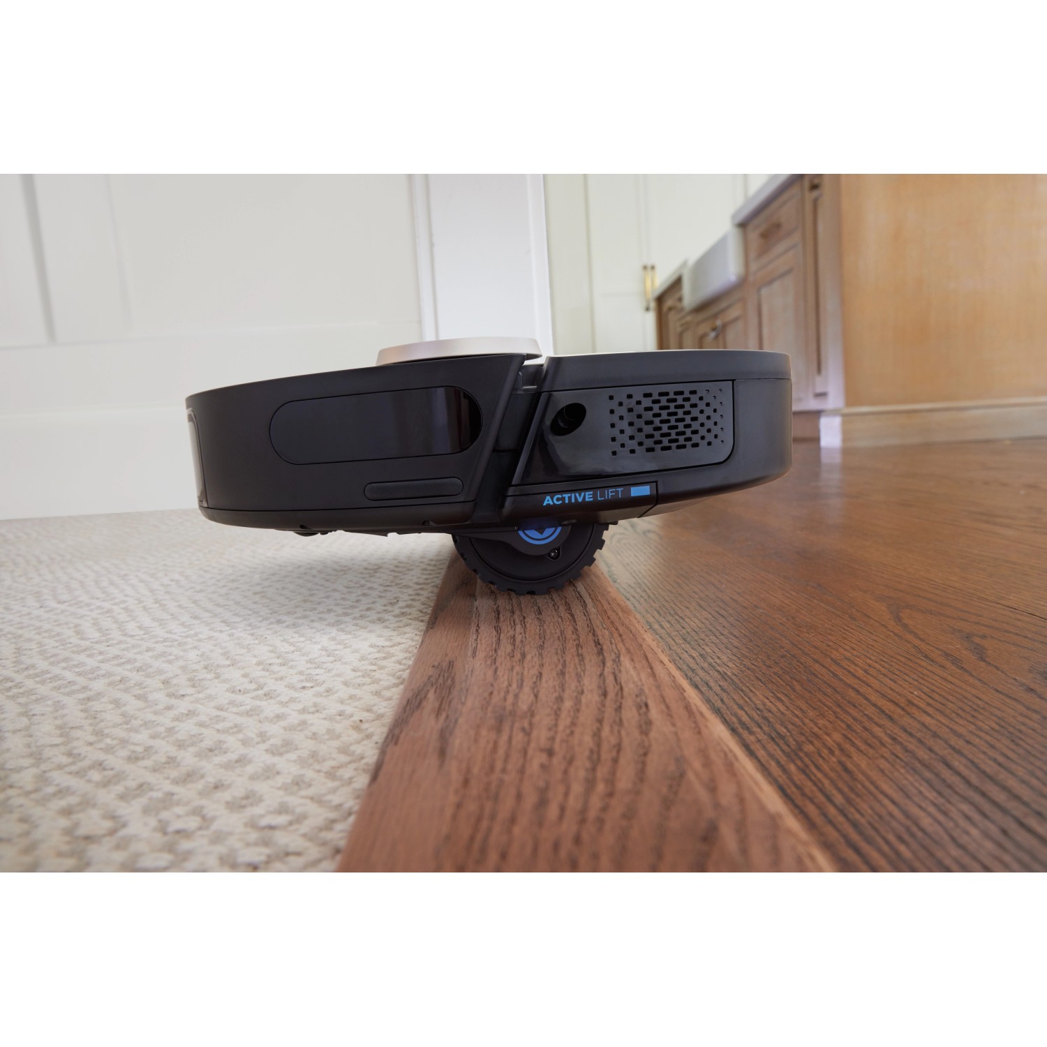 Shark Saugroboter Power Detect RV2820VEEU überwindet einen Absatz zwischen Teppich und Holzboden.