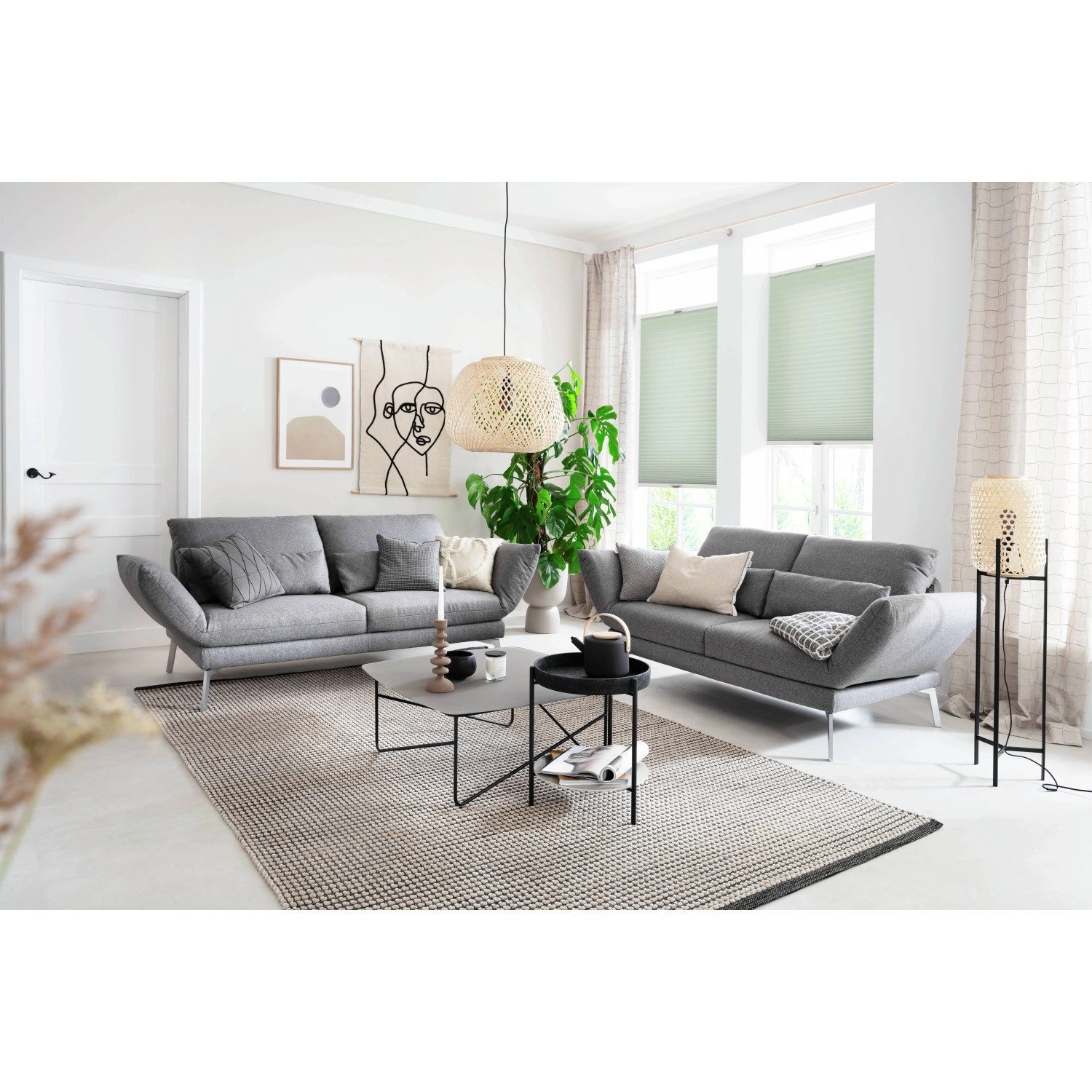 Helle Wohnraum-Szene mit grauen Sofas und grünem Schöner Wohnen Plissee Milla (90x130 cm) am Fenster.