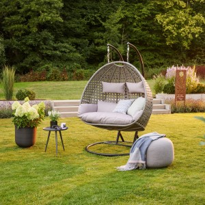 Grauer Home Deluxe Hängesessel Twin Polyrattan mit Kissen im Garten.