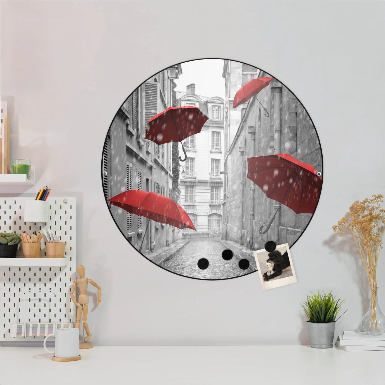 Runde, schwarze Magnettafel mit Motiv roter Schirme vor grauer Stadtkulisse als Wanddekoration.