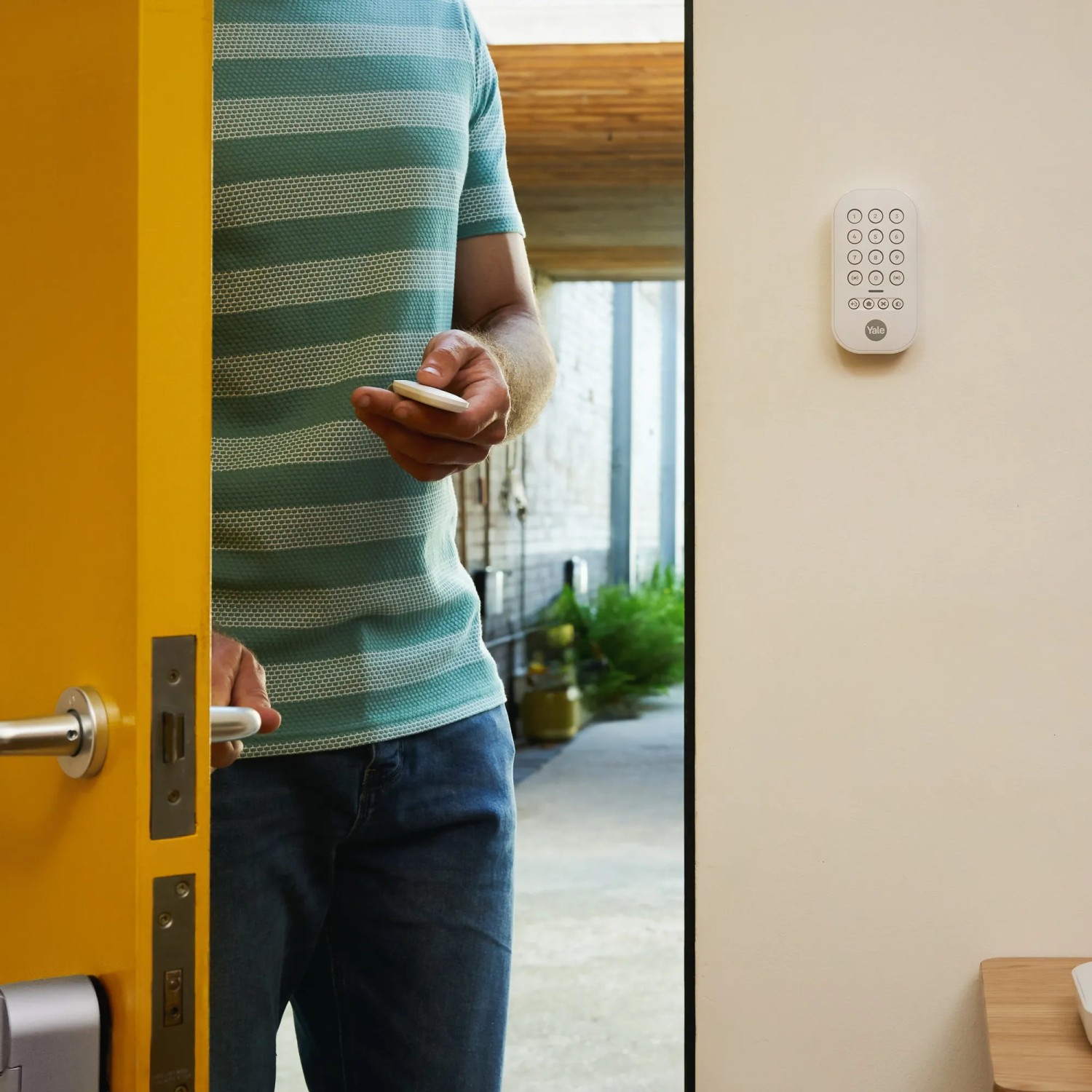 Mann öffnet Tür mit Yale Fernbedienung für Smart Alarm Alarmanlage in Weiß.
