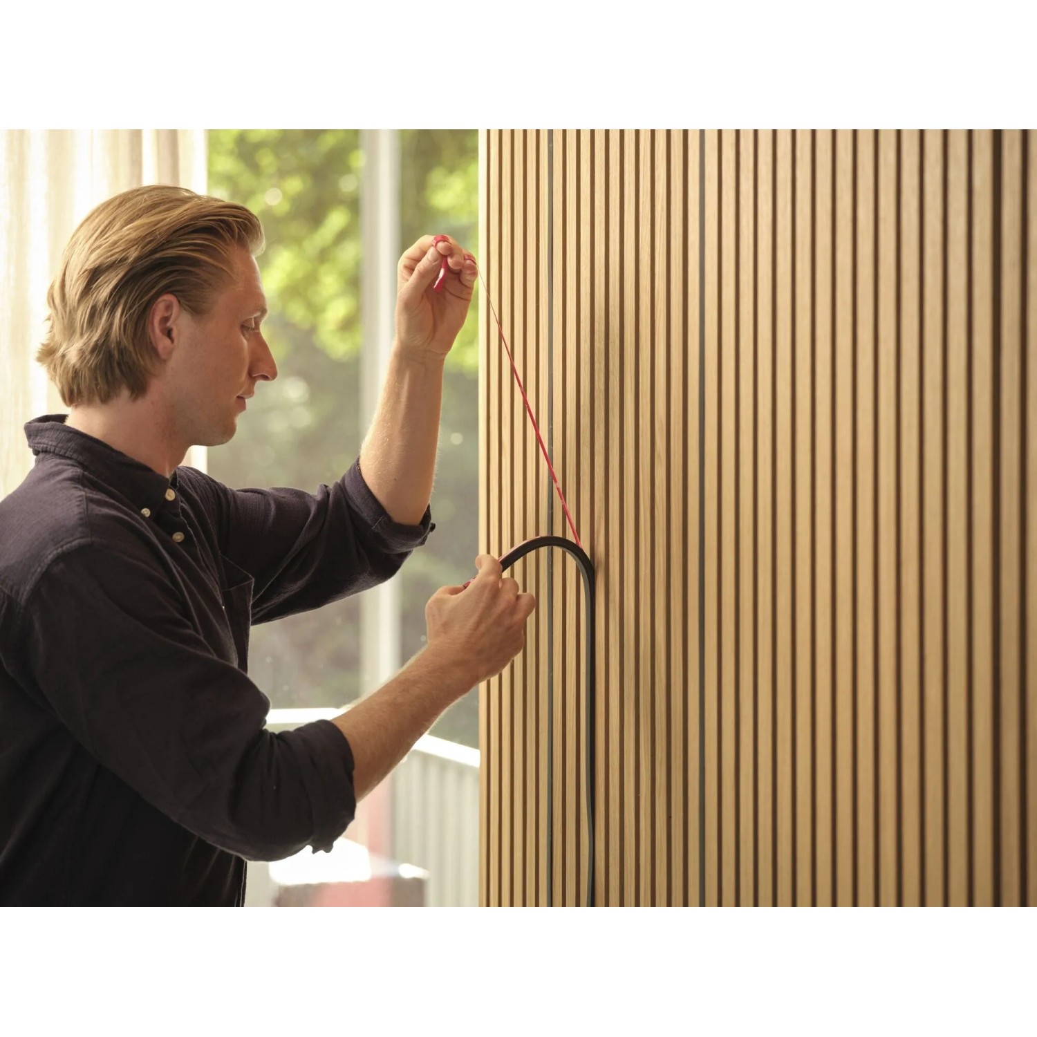 Mann installiert schwarzen OSRAM Acoustic LED Streifen in Holz-Akustikpaneel. Das Starter-Set ist für einfache Anbringung.